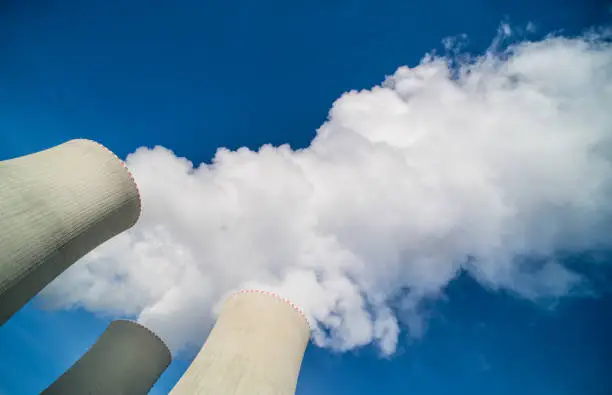 Photo of Top of nuclear power plant water cooling towers with white steam plume on a blue sky