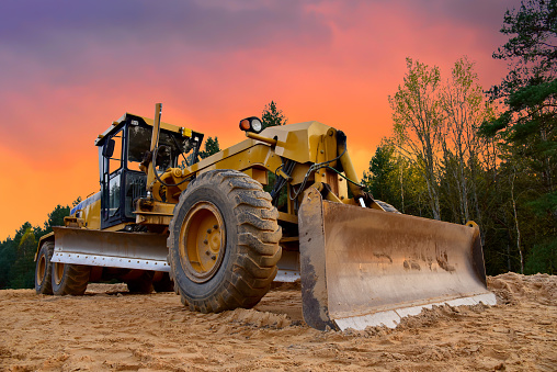 Motor Grader en la construcción de carreteras en área forestal. Greyder nivelación de la arena, el suelo y la grava durante el trabajo en carretera photo
