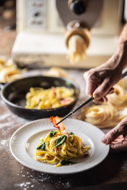 istock Hands of chef plating freshly cooked pasta with a pasta maker in the background. 1289166006