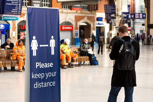 London, UK - 1 December, 2020: a large sign in Victoria railway station in central London, UK, encourages people to maintain social distance during the coronavirus pandemic. People and commuters are defocused in the background.