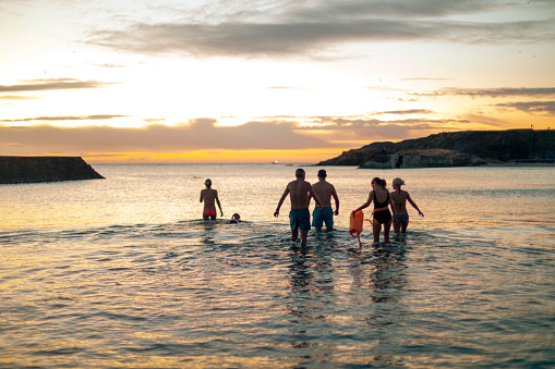 Rear view of a group of friends walking out into the ocean while open water swimming at dawn.