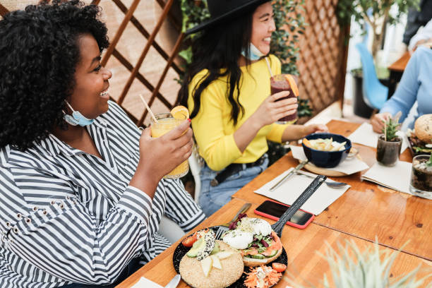 istock Multiracial young women eating brunch during coronavirus outbreak - Girls wearing protective masks at trendy restaurant - Healthy lifestyle and social distance concept - Focus on asian female face 1289171605