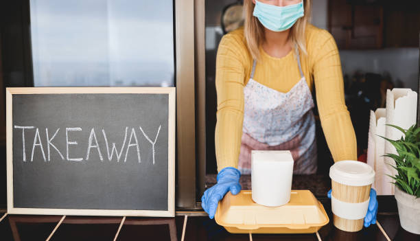 istock Young woman preparing takeaway organic food inside restaurant during Coronavirus outbreak - Worker inside kitchen cooking food for delivery service wearing safety mask - Focus on face 1289175080