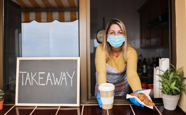 istock Young woman wearing face mask while serving takeaway breakfast and coffee inside bakery cafe 1289175098