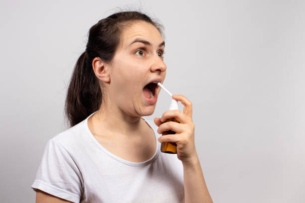 istock A patient sprays a coughing agent into his throat - an antiseptic against laryngitis and pharyngitis. Medications, therapy and treatment of a sick, asthma. Spray medicine in the mouth 1289176865