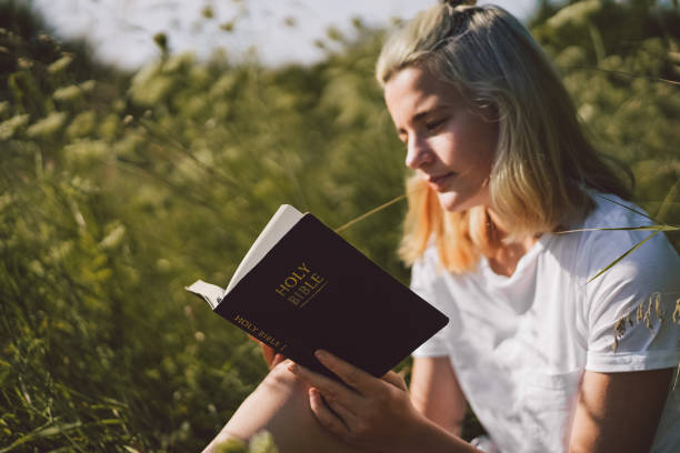 adolescente cristiana che legge la bibbia sul campo. concetto di fede, spiritualità e religione - please god foto e immagini stock