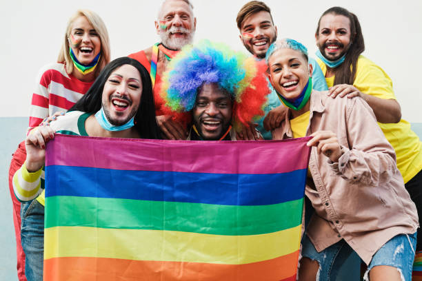 istock Gay people dance at pride parade with LGBT flags while wearing protective face mask - Main focus on bottom guys faces 1289177172