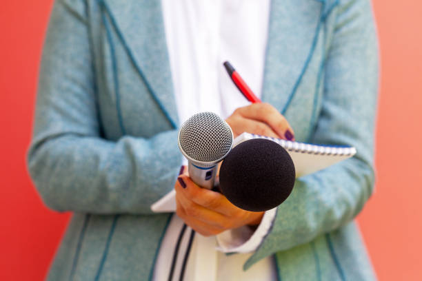 istock Female journalist at news conference, writing notes, holding microphone 1289177219