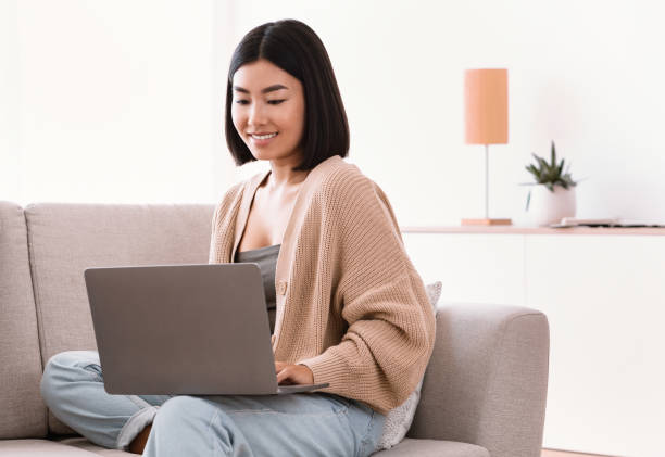 istock Asian woman sitting on couch and working on computer 1289177340
