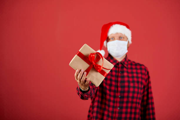 istock Man in protective face mask and Santa hat with Christmas DIY gift 1289178642