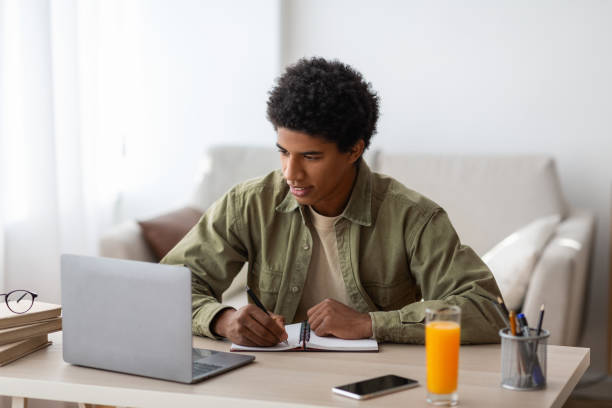istock Homeschooling concept. Black student writing in copybook during online conference or web lesson at home 1289178659