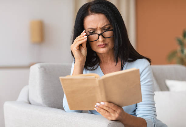 istock Mature woman touching glasses trying to read book 1289179414