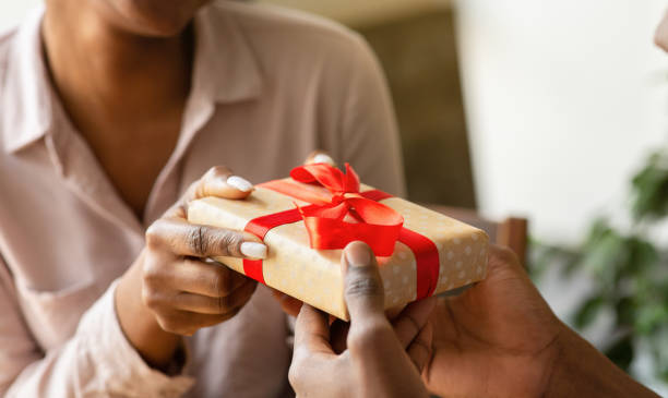 un tipo negro irreconocible dando a su novia regalo de cumpleaños en el café, primer plano de manos - regalo fotografías e imágenes de stock
