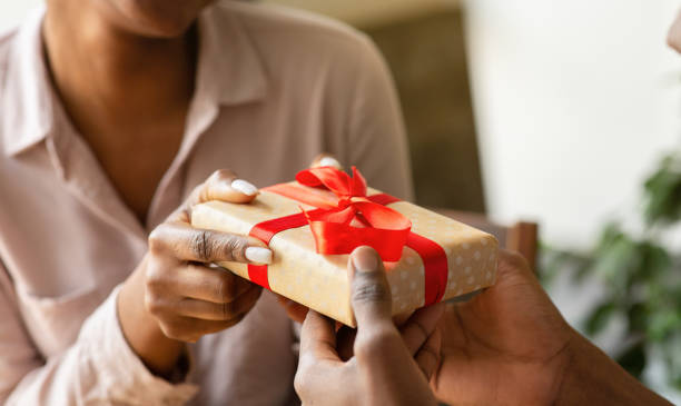 Unrecognizable black guy giving his girlfriend birthday gift at cafe, closeup of hands Unrecognizable black guy giving his girlfriend birthday gift at cafe, closeup of hands. Romantic young couple celebrating holiday together at coffee shop, exchanging presents with each other anniversary gifts stock pictures, royalty-free photos & images