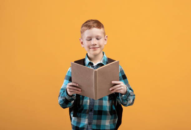 istock Joyful schoolboy reading book, yellow studio background 1289180609
