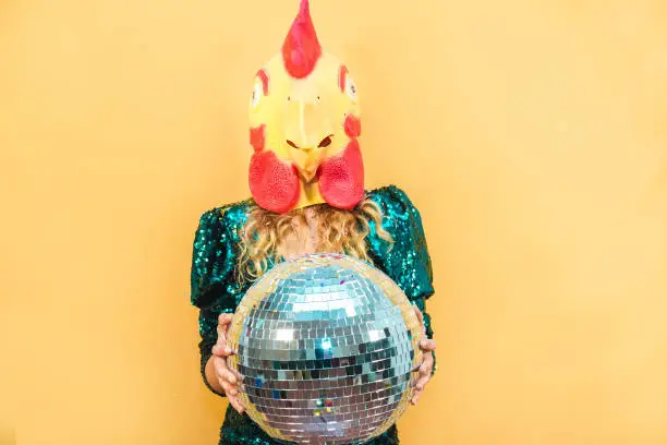 Photo of Young woman wearing chicken mask while holding disco ball at new year's party - Soft focus on face