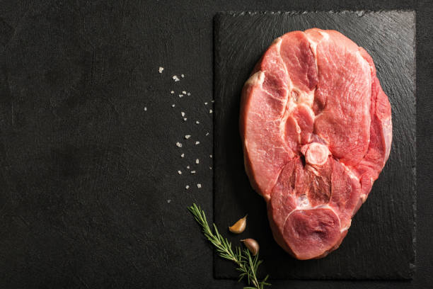istock Uncooked Pork Ham steak on a stone kitchen cutting board. 1289185117