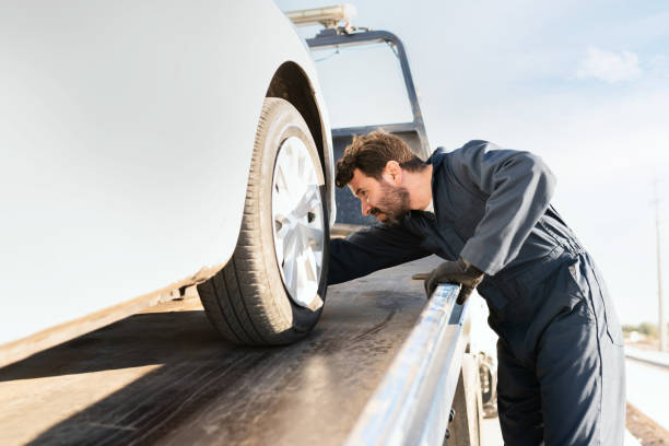 Tow truck worker securing the car on the platform Side view of an operator checking on a broken-down vehicle on the plataform of the tow truck tow truck stock pictures, royalty-free photos & images