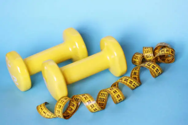 Photo of Yellow dumbbells and measure tape on blue background