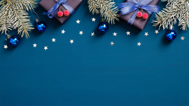 istock Merry Christmas and Happy Holidays greeting card design with pine tree branches, gift boxes and confetti on dark blue background. Flat lay, top view. 1289188752