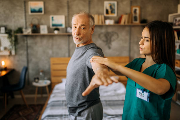 Senior adult man and home healthcare nurse, physical therapist Senior adult, male patient does arm exercises with home healthcare nurse or physical therapist in nursing home or home setting occupational therapy photos stock pictures, royalty-free photos & images