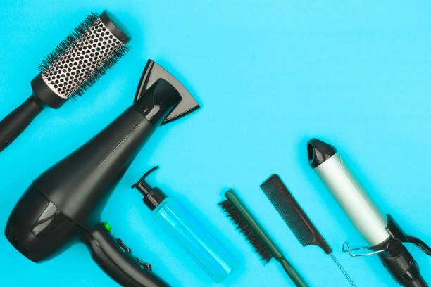 istock Hairdressing tools in black: hairdryer, combs, sprays, curling iron on a blue background, space for text, flat lay. 1289189196