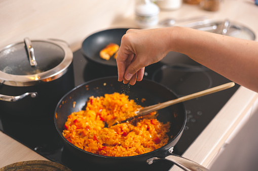 Woman's hand seasoning fried rice with vegetables in frying pan