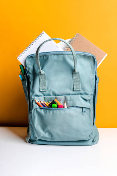 istock Blue backpack with different colorful stationery on a yellow background. Banner design 1289191127