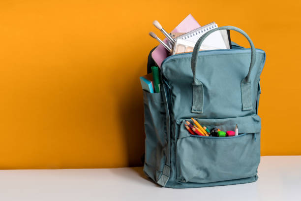 istock Blue backpack with different colorful stationery on a yellow background. Banner design 1289191209
