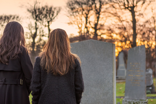 Two mourning persons standing in front of a grave at the graveyard.