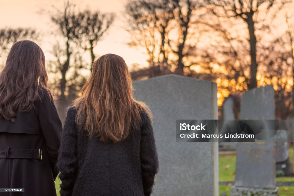 A visit to the graveyard Two mourning persons standing in front of a grave at the graveyard. Grief Stock Photo