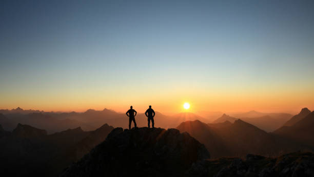 istock Two Men reaching summit enjoying freedom and looking towards mountains sunset. 1289191537