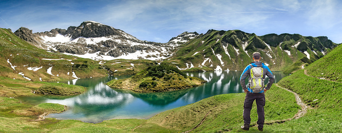 Hiker Man with Backpack watching remote Schrecksee lake up high in the alpine mountains in spring or summer. Bavaria, Allgau, Germany.