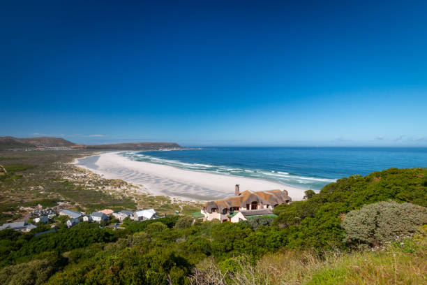 Panorama view of Noordhoek beach near Cape Town, South Africa Panorama view of Noordhoek Long Beach with white sand near Cape Town, South Africa against blue sky. Seen from Chapmans Peak Drive. The town of Kommetjie with its beautiful lighthouse is located at the back end of the beach kommetjie stock pictures, royalty-free photos & images