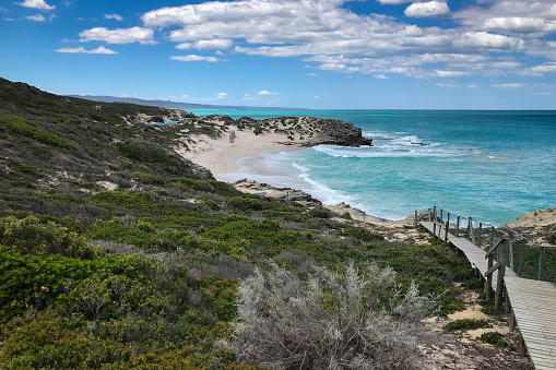 Scenic view of wooden footpath walkway leading to through sand dunes with fynbos vegetation to beautiful Indian Ocean beach at coast of De Hoop nature reserve, South Africa against sky