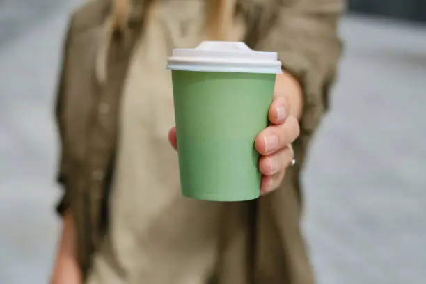 Green paper cup with coffee in woman hand. Time for drink coffee in city. Coffee to go. Enjoy moment, take a break. Disposable paper cup closeup. Delicious hot beverage. Blank space for text, mockup