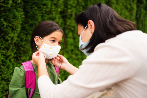 istock Young woman putting a protective mask on her daughter`s face during COVID-19 1289197077