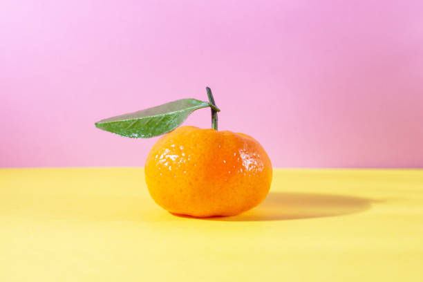 istock Ripe orange tangerine with leaf on pink and yellow background 1289206431