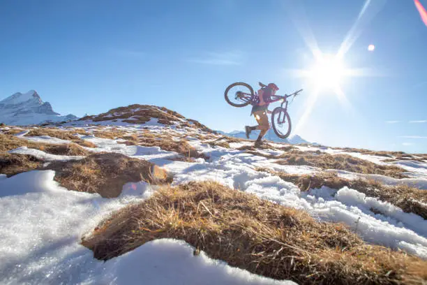 Photo of Young man carries mountain bike up snowy hill in the morning