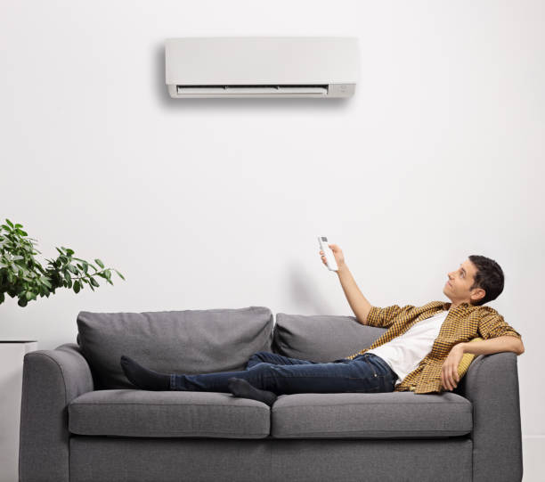 istock Young man laying on a sofa with a remote control setting the air conditioning unit 1289209163