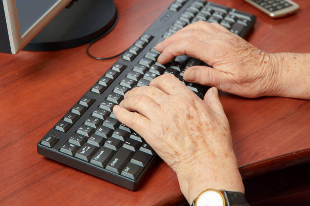 Hands of an elderly woman who types on a computer keyboard stock photo