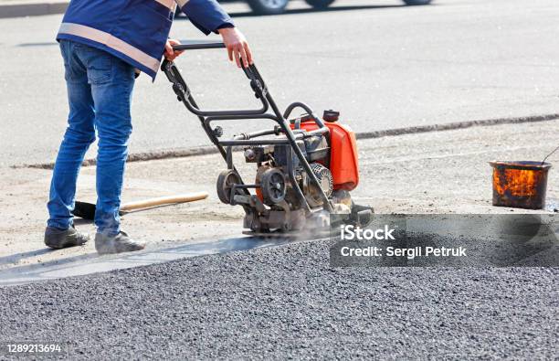 A Road Service Worker Repairs The Roadway By Compacting The Asphalt With A Plate Petrol Vibrator Stock Photo - Download Image Now
