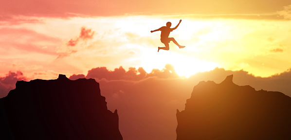 Hombre saltando sobre el precipicio entre dos montañas rocosas al atardecer. Libertad, riesgo, desafío, éxito photo