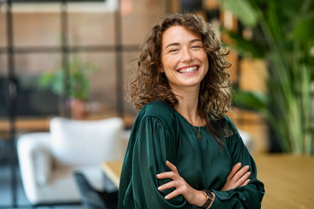 Beautiful woman smiling with crossed arms Portrait of young smiling woman looking at camera with crossed arms. Happy girl standing in creative office. Successful businesswoman standing in office with copy space. charming stock pictures, royalty-free photos & images