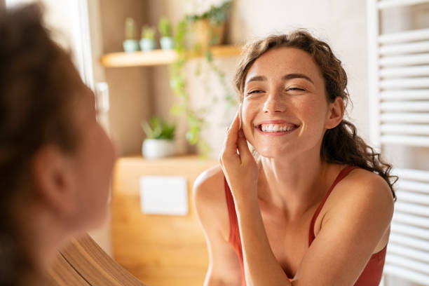 Beauty woman using cotton pad to remove make up Cheerful young woman using cotton pad while looking in mirror. Happy smiling beautiful girl cleaning skin with cotton pad. Beauty natural woman looking in mirror while cleansing skin face and using cosmetic products for properly deep clean. exfoliation photos stock pictures, royalty-free photos & images