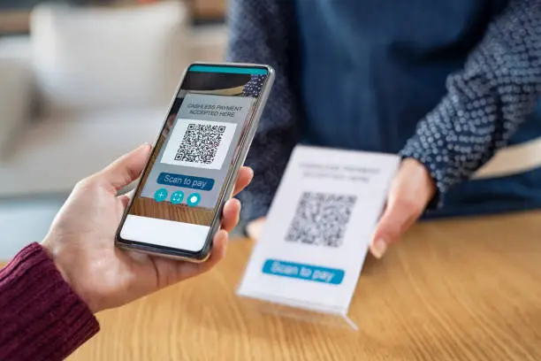 Close up of young woman hand holding smartphone and scanning qr code for digital payment. Customer paying money online using mobile phone after shopping. Girl using cellphone scanner to scan qr code in a coffee shop.