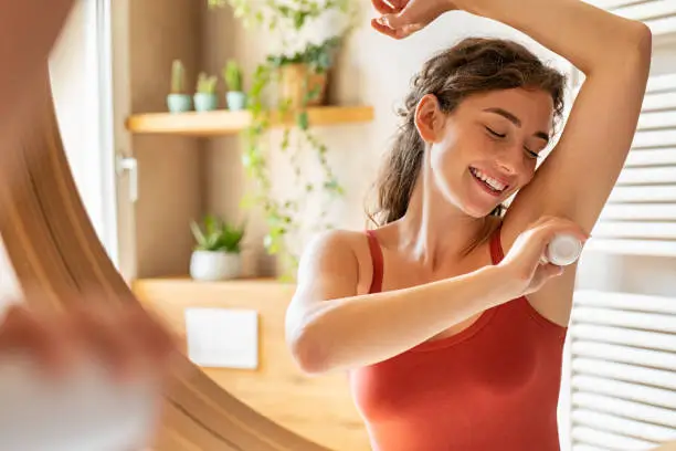 Photo of Happy young woman using roll on deodorant