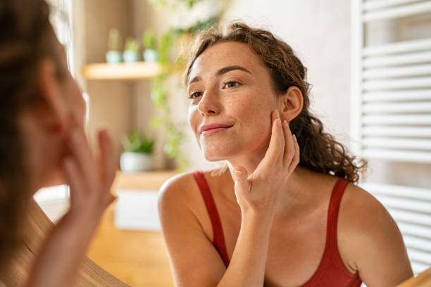 молодая женщина красоты проверки ее кожи в зеркало по утрам - moisturizer beauty treatment human skin applying стоковые фото и изображения