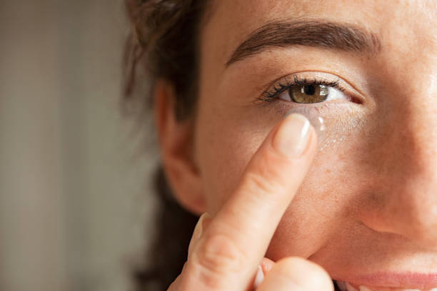 mujer poniéndole lentes de contacto en el ojo - insertar fotografías e imágenes de stock