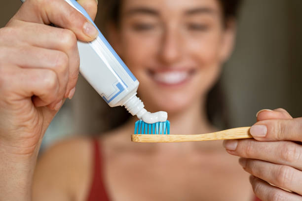 Woman applying toothpaste on bamboo toothbrush Close up of woman with tooth brush applying paste in bathroom. Closeup of girl hands squeezing toothpaste on ecological wooden brush. Smiling beautiful woman applying toothpaste on eco friendly toothbrush. toothpaste stock pictures, royalty-free photos & images